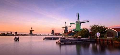 Traditionelle niederländische Windmühlen und Holzhäuser am Wasser in Zaanse Schans während des Sonnenuntergangs