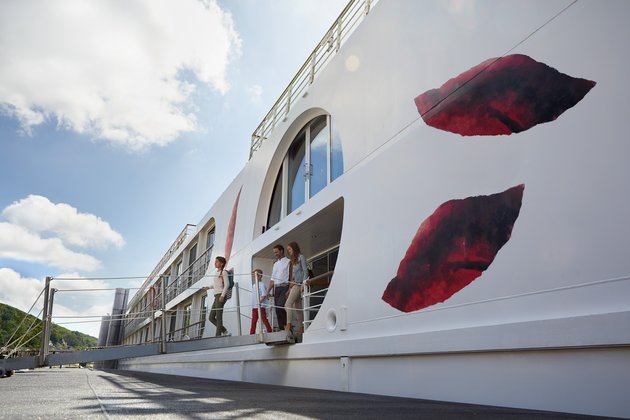A family with two children disembarks from a white river cruise ship onto a landing stage via a gangway.