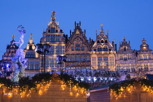 Christmas-decorated marketplace in Antwerp with illuminated stalls at dusk.