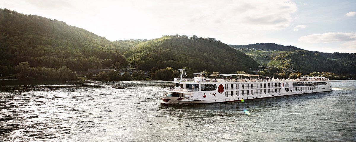 In the afternoon, the A-ROSA BRAVA glides along the Rhine, with green, wooded hills and small villages in the background on the shore.
