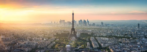 View of the Eiffel Tower in Paris at sunset, surrounded by trees and buildings, with a clear sky in the background.