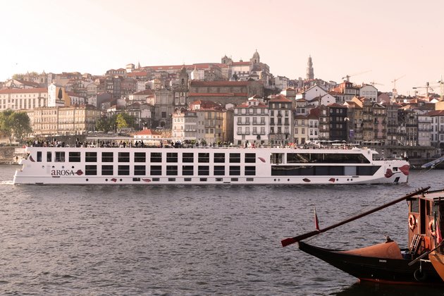 River cruise ship A-ROSA ALVA on the Douro in front of a city with historic buildings and red roofs.