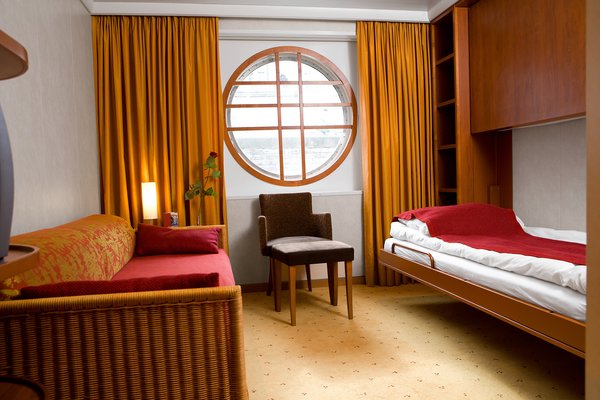 A cabin of category S on board the A-ROSA LUNA and A-ROSA STELLA. Furnished in warm colors with two single beds and portholes as windows. On the wall is a Pullman bed that can be folded down.