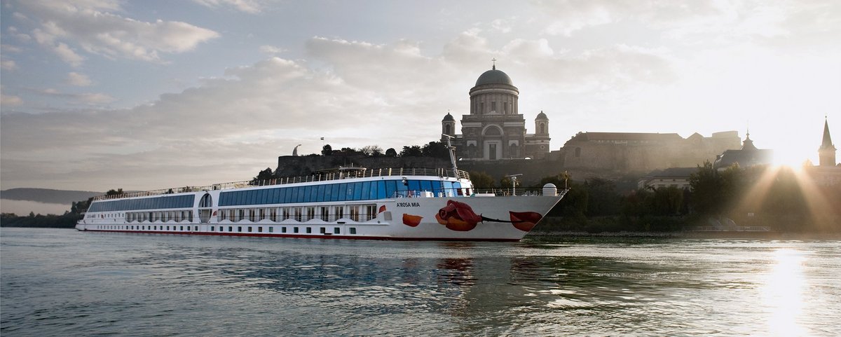 The river cruise ship A-ROSA MIA sails past Esztergom on the Danube with the St. Adalbert Cathedral at sunrise.