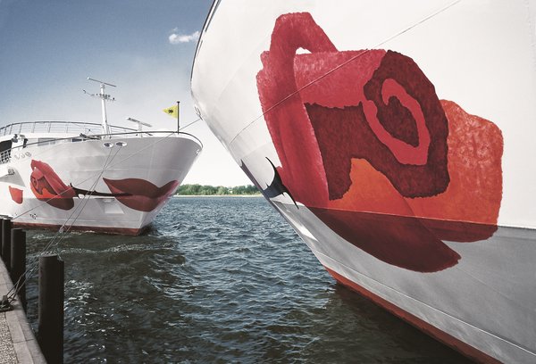 Close-up of a river cruise ship in the A-ROSA fleet with a distinctive rose on the bow in the foreground. Opposite is a second A-ROSA ship with a view of the bow.