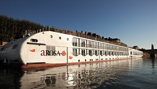 The A-ROSA STELLA is moored on the bank in a city on the Rhône at sunrise, with a bridge and buildings in the background.