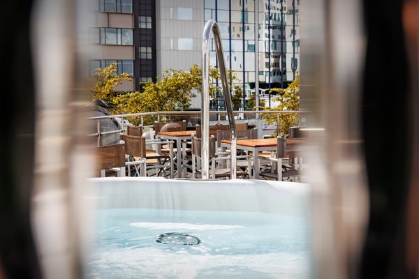 The whirlpool on the sundeck in the sunlight, with seating areas in the background with a view of modern buildings.