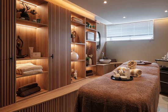 Stylish treatment room with warm lighting, shelves with decorations and care products, as well as a treatment table.