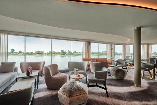 Modern lounge on board the A-ROSA SENA with comfortable seating, stylish lighting, and floor-to-ceiling windows overlooking the river.
