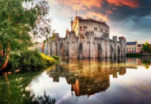 Burg Gravensteen in Gent, Belgien, mit mittelalterlicher Architektur und Türmen, umgeben von Wassergraben und Bäumen.