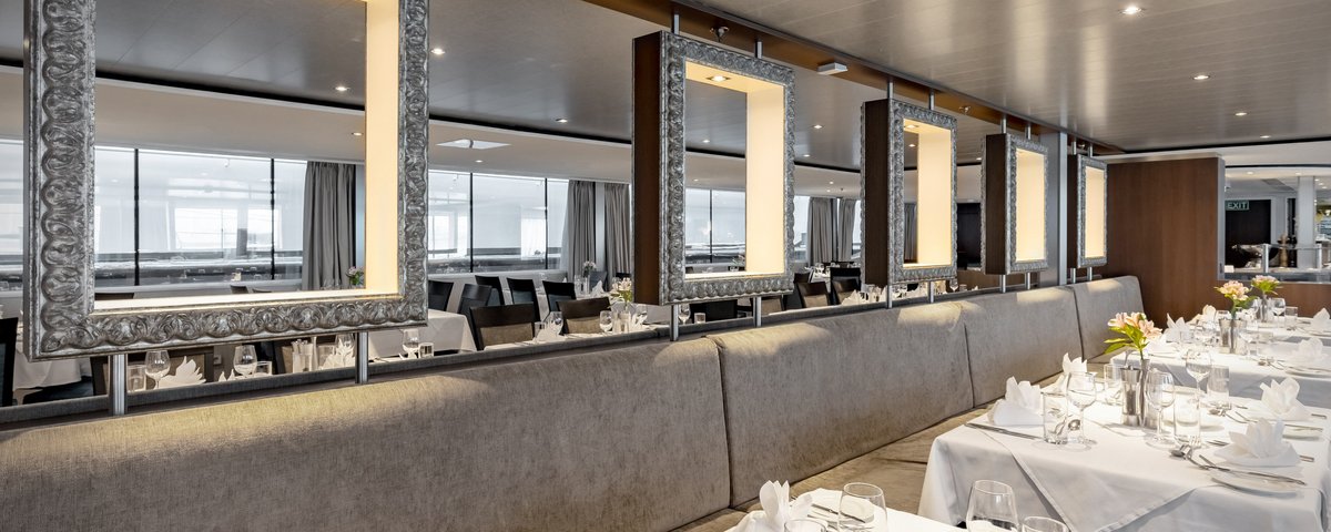 Stylishly set restaurant area of the A-ROSA ALEA with windows, floral decorations, and dimmed lighting.