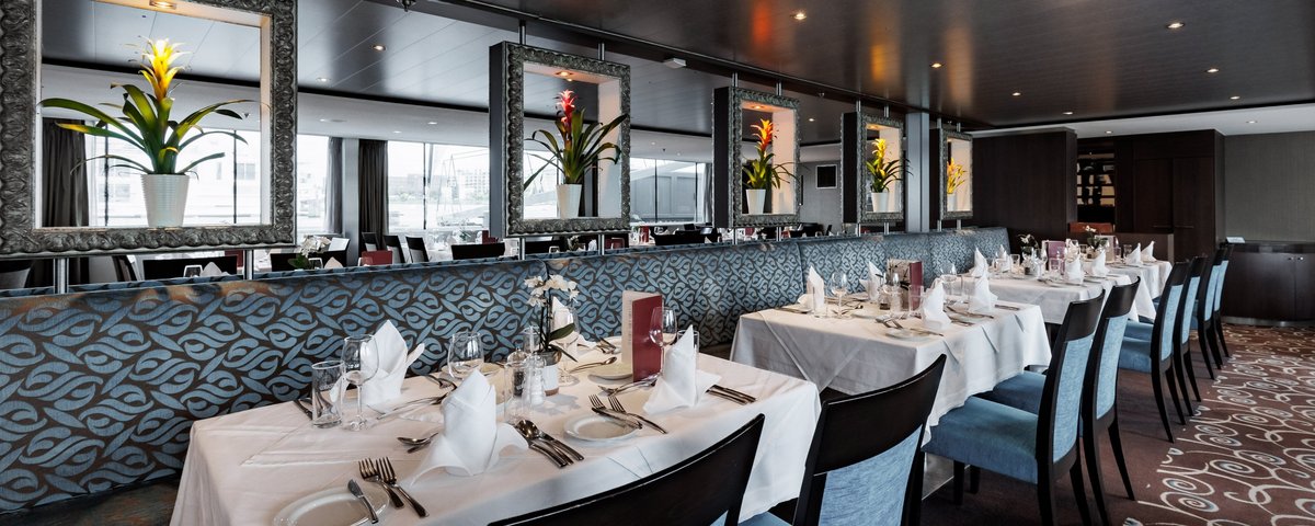 Stylishly set restaurant area of the A-ROSA CLEA with windows, floral decorations, and dimmed lighting.