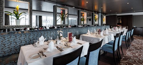 Stylishly set restaurant area of the A-ROSA CLEA with windows, floral decorations, and dimmed lighting.