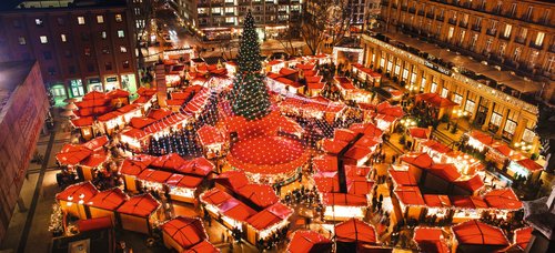 Christmas market in Cologne at night with festively lit stalls, a large Christmas tree, and people strolling through the market.