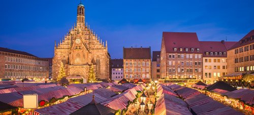Weihnachtsmarkt in Nürnberg bei Nacht, mit festlich beleuchteten Ständen und einem großen, geschmückten Weihnachtsbaum im Hintergrund.