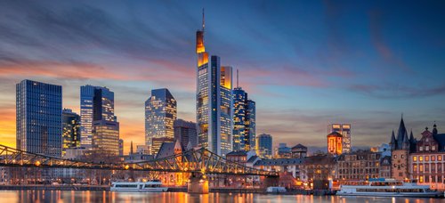 Skyline von Frankfurt am Main mit modernen Hochhäusern und dem Main im Vordergrund bei Sonnenuntergang.