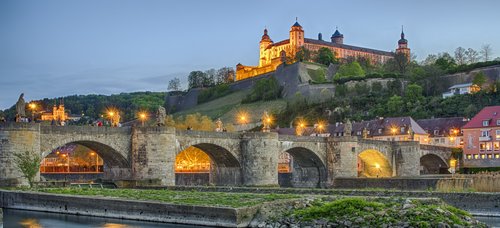 Blick auf die Festung Marienberg in Würzburg, umgeben von grünen Weinbergen und dem Main, bei Abenddämmerung