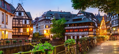Straßburger Altstadt mit Fachwerkhäusern umgeben von Bäumen und einem Fluss bei Abenddämmerung.