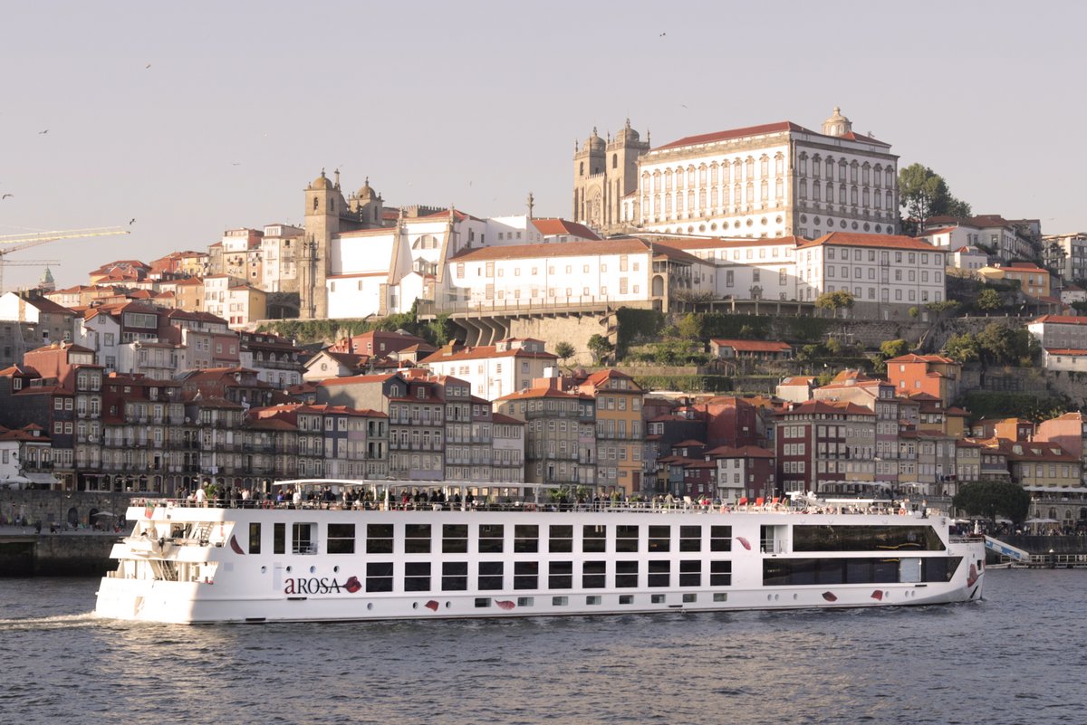 River cruise ship A-ROSA ALVA on the Douro in front of a city with historic buildings and red roofs.