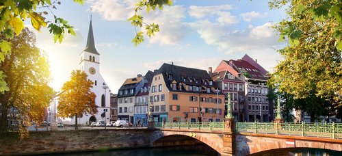 Straßburger Altstadt mit Fachwerkhäusern und der Kathedrale im Hintergrund, umgeben von Bäumen und einem Fluss bei Sonnenuntergang.