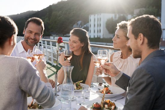Yvonne Catterfeld and four other people are sitting at dinner with wine on the sun deck, sunlight in the background.
