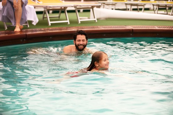 A family enjoys the pool on the deck of a river cruise ship, surrounded by deck chairs and sun umbrellas.
