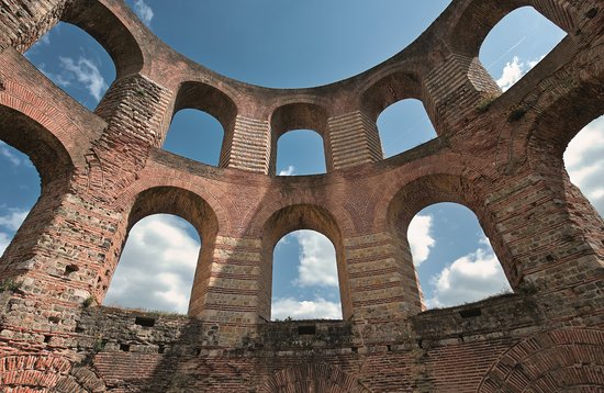 Ruins of the Imperial Baths in Trier, with ancient stone walls and arches, with a blue sky in the background.