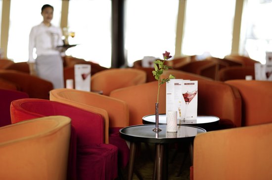 Seating area in the lounge on the A-ROSA DONNA with comfortable armchairs at a table with a rose on it and a waitress with drinks in the background.