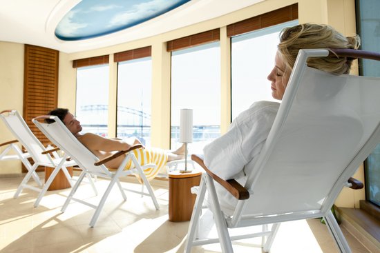 Two people are relaxing on the deck chairs in the relaxation area of SPA-ROSA, in front of them floor-to-ceiling windows with a view of the river.