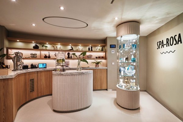 Reception area of the SPA-ROSA with decorative shelves, marble island, and glass display case with products next to a staircase.