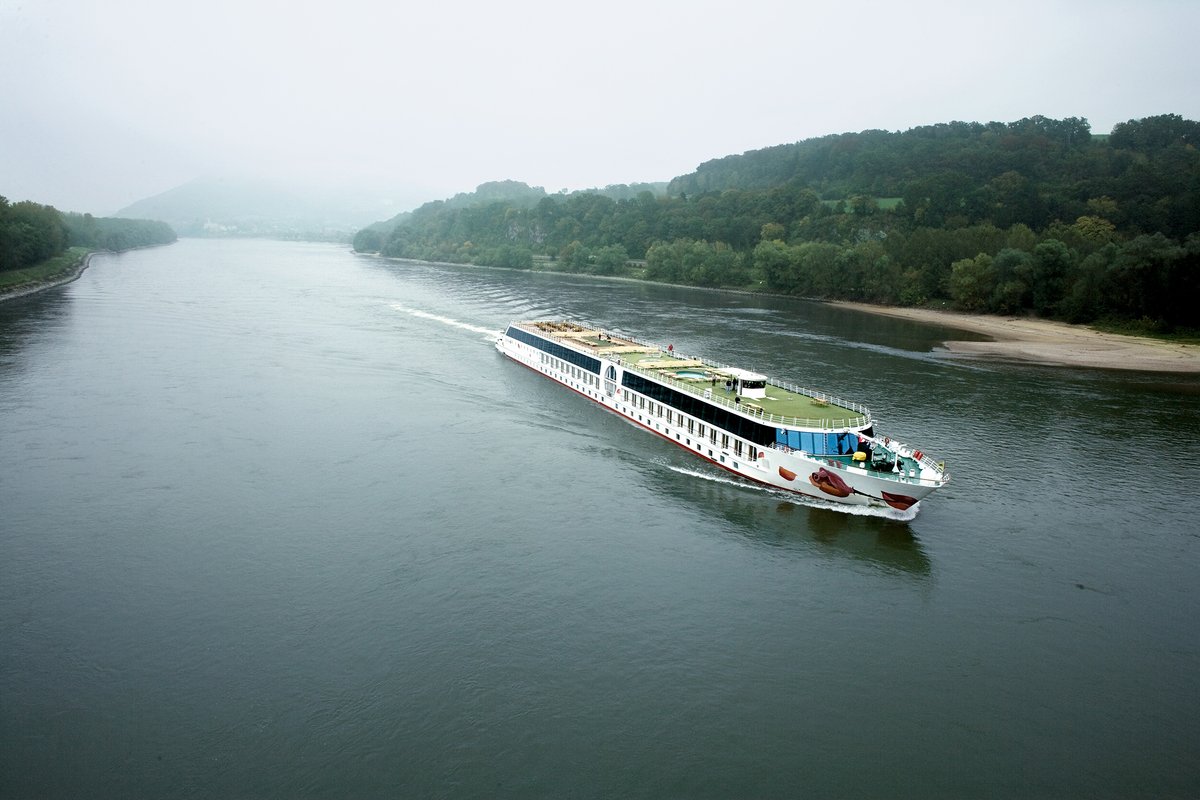 The river cruise ship A-ROSA MIA on the Danube through the Wachau, surrounded by the calm river and the densely vegetated shore with misty hill landscape.