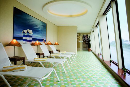The relaxation room in the spa area on a river cruise ship of the A-ROSA fleet with relaxation loungers with towels and a view through the panoramic windows of the Danube.
